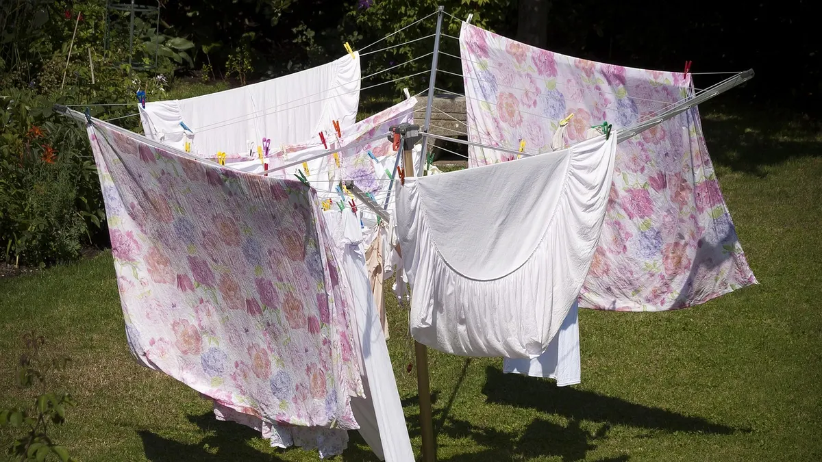 Lençóis estampados e roupas brancas secando em varal no jardim